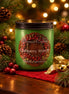 Cranberry Wreath Candle in a green jar surrounded by holiday decorations and pinecones with festive lights in the background.