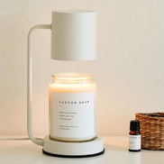 White arched candle warmer lamp with a white shade above a clear jar candle, styled with dried botanicals on a light surface.
