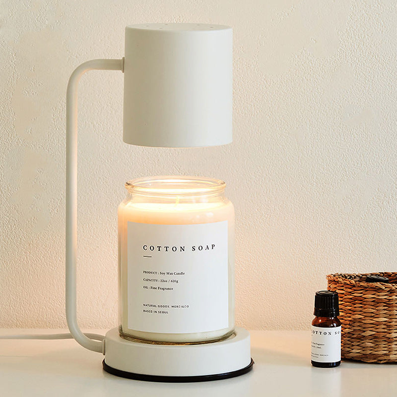 White arched candle warmer lamp with a white shade above a clear jar candle, styled with dried botanicals on a light surface.