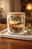 Frosted glass candle jar with round wooden lid labeled "Enchanted Forest" featuring a mushroom-forest photo, on a marble tray over a wood table.