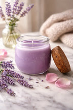 Falling For You Candle in a glass jar with a wooden lid, lavender flowers, and rose petals on a marble surface.