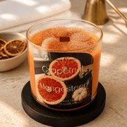 Clear glass jar candle with orange wax, grapefruit-segment toppers and a square wooden wick; label reads 'Grapefruit Mangosteen'.