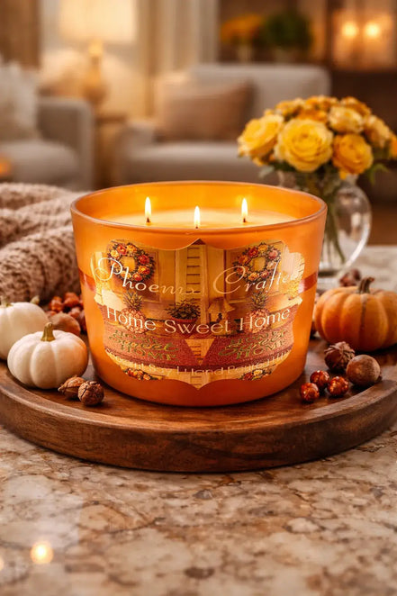 Three-wick amber glass Home Sweet Home candle on a wooden tray with small white and orange pumpkins and nuts.