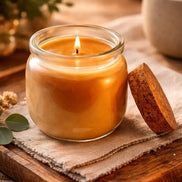 Home Sweet Home Candle in a glass jar with a cork lid, glowing warmly on a wooden surface with soft textiles and greenery.