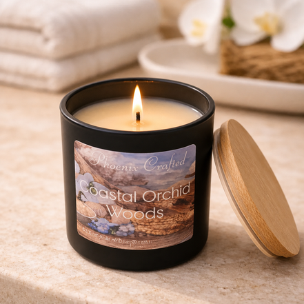 Lit beige wax candle in a matte black jar labeled Phoenix Crafted Coastal Orchid Woods.