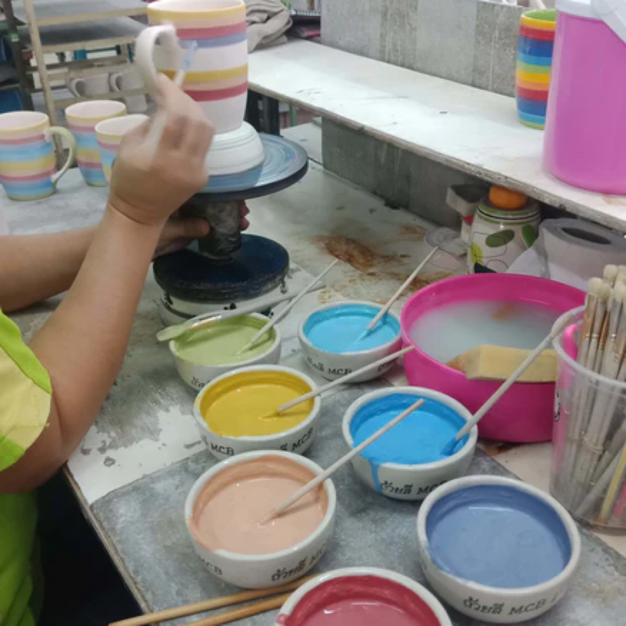 Person painting a ceramic Rainbow Wax Melt Essential Oil Burner Warmer with colorful paint pots in a pottery studio.