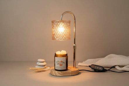 Chrome lamp warmer with patterned glass shade over a wood base holding an amber jar with white wax chunks; black remote.
