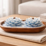 Island Orchard blue-and-white lotus-shaped decorative candles with short wooden wicks in an oval wooden bowl on a folded cream cloth.