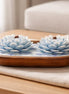 Island Orchard blue-and-white lotus-shaped decorative candles with short wooden wicks in an oval wooden bowl on a folded cream cloth.