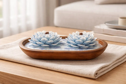 Island Orchard blue-and-white lotus-shaped decorative candles with short wooden wicks in an oval wooden bowl on a folded cream cloth.