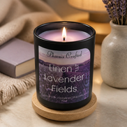 Lit Linen & Lavender Fields candle in a matte black jar on a wooden coaster beside lavender sprigs and a book.