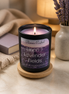 Lit Linen & Lavender Fields candle in a matte black jar on a wooden coaster beside lavender sprigs and a book.