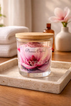 Magnolia Candle in a glass jar with wooden lid, featuring pink petals, on a stone tray.