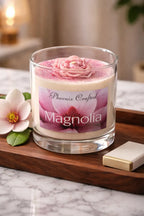 Magnolia Candle in a glass container with pink floral decoration and elegant label on a wooden tray.