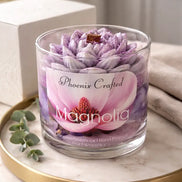 Phoenix Crafted Magnolia candle in a clear glass jar with a purple-and-white lotus-shaped wax topper and wooden wick on a marble tray.