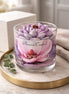 Phoenix Crafted Magnolia candle in a clear glass jar with a purple-and-white lotus-shaped wax topper and wooden wick on a marble tray.