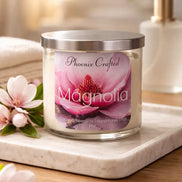 Clear glass jar candle with silver lid and Phoenix Crafted Magnolia label, white wax on a marble tray with pink magnolia blossoms.