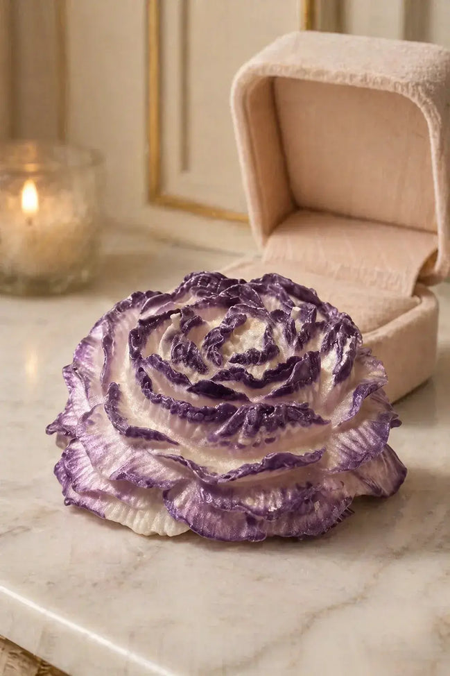 Magnolia Candle in a floral-shaped design, featuring purple and white layers, set on a marble surface with a candle.