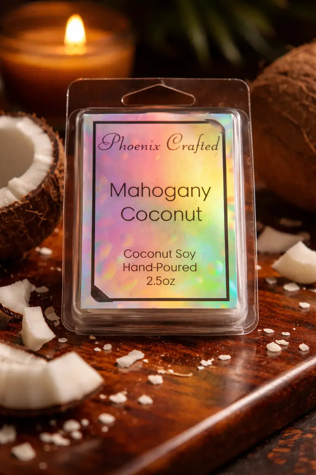 Clear clamshell wax melt pack with holographic label reading “Phoenix Crafted” and “Mahogany Coconut,” on a wooden board with coconut halves, flakes.