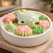 Mahogany Teakwood Candle with Decorative Lizard and succulent arrangement in a round bowl with pink and green flowers.