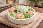 A decorative dessert featuring a hedgehog, flowers, and greenery, beautifully arranged in a white bowl.