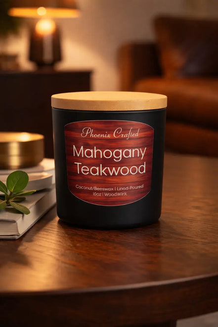 Black jar candle with a light wood lid and red wood-grain label reading "Phoenix Crafted" and "Mahogany Teakwood" on a wooden table