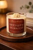Glass jar candle with cream-colored wax and piped topper labeled "Phoenix Crafted Mahogany Teakwood" on a round wooden tray.