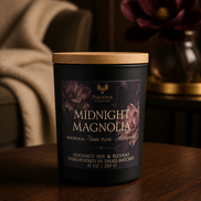 Midnight Magnolia candle in a matte black jar with a wood lid on a wood table beside a magnolia flower.