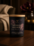 Midnight Magnolia candle in a matte black jar with a wood lid on a wood table beside a magnolia flower.