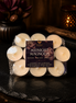 Midnight Magnolia tealights in clear packaging around a Midnight Magnolia product card on a dark stone surface.