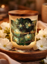 Frosted glass jar candle with wooden lid, labeled 'Phoenix Crafted Moonflower Rain' on a green floral label.