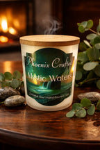 Mystic Waters Candle with a wooden lid, hand-poured coconut soy, surrounded by greenery and stones, burning softly.