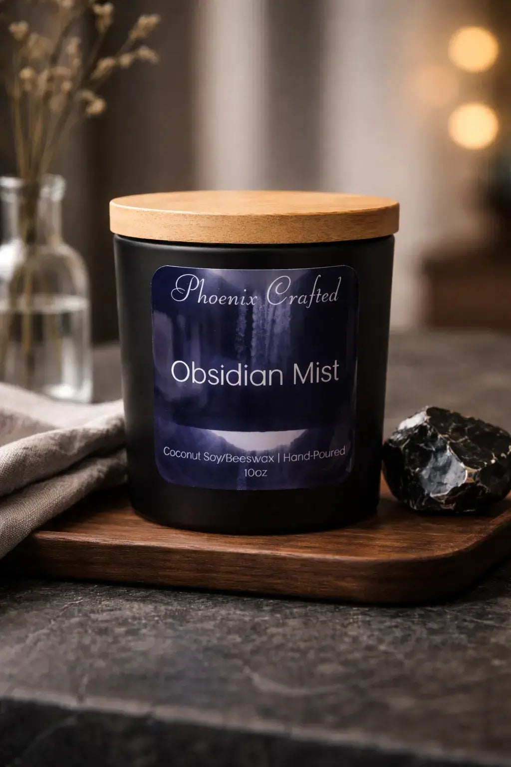 Obsidian Mist Candle displayed on a wooden tray with a raw obsidian stone beside it, featuring a minimalist black jar.