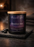 Black glass candle jar with light wooden lid and purple label 'Phoenix Crafted - Obsidian Mist' on textured slate with black stones and smoke.