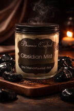 Obsidian Mist Candle in a glass jar with smoky fragrance, surrounded by polished obsidian stones.