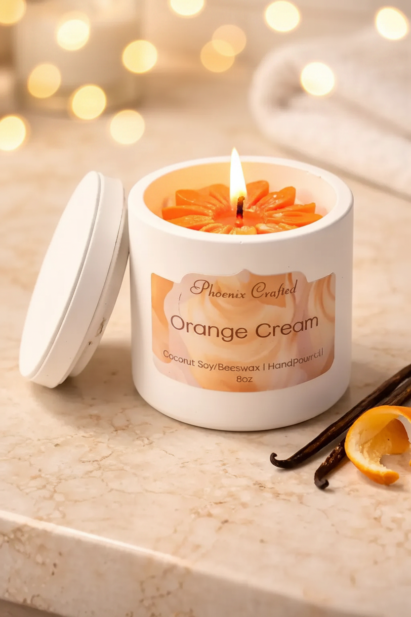 White jar candle labeled 'Phoenix Crafted Orange Cream' with lid beside it.