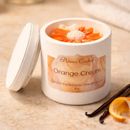 Orange Cream Candle in a white jar with orange decorations and vanilla pod on a marble surface.