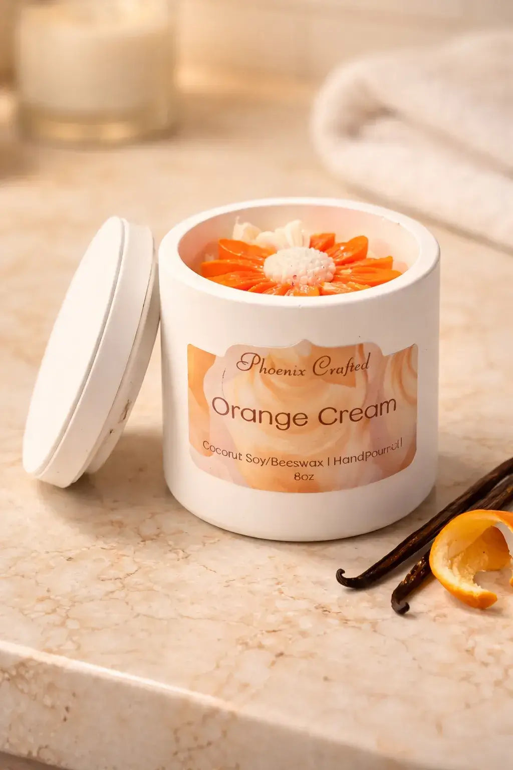 Orange Cream Candle in a white jar with orange decorations and vanilla pod on a marble surface.
