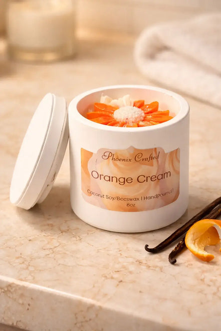 Orange Cream Candle in a white jar with orange decorations and vanilla pod on a marble surface.