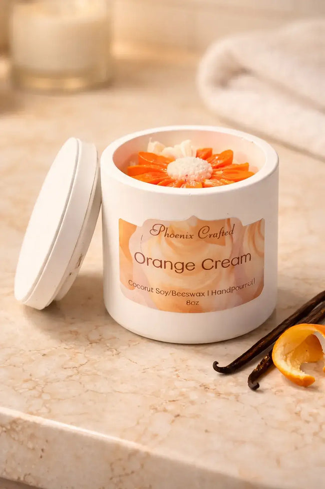 Orange Cream Candle in a white jar with orange decorations and vanilla pod on a marble surface.
