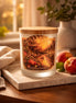 Frosted glass jar candle with a wooden lid and illustrated 'Peach Paradise' label, fresh peaches on a stone tray in warm window light
