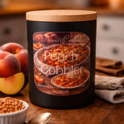Black cylindrical candle jar with light-colored lid and label Peach Cobbler showing peaches, a ramekin of crumble and a spoon on a table.
