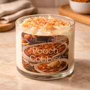 Clear round glass candle with white whipped wax and peach crumble topping labeled 'Phoenix Crafted' and 'Peach Cobbler'.
