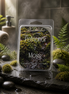Petrichor & Moss wax melts in a clear clamshell with a mossy woodland label, styled with ferns and dark stones.