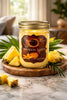 Pineapple Eclipse Candle in a glass jar surrounded by fresh pineapple on a wooden surface.