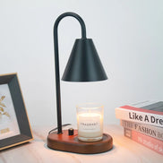 Black arched candle warmer lamp with a dark conical shade and round wood base, styled with a clear jar candle, books, and framed art.