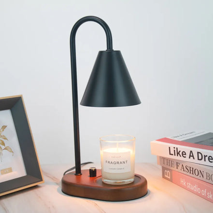 Black arched candle warmer lamp with a dark conical shade and round wood base, styled with a clear jar candle, books, and framed art.