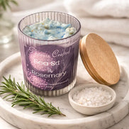 Sea Salt & Rosemary Candle in a glass jar with a wooden lid on a marble tray alongside fresh rosemary and sea salt.