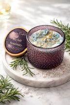Sea Salt & Rosemary Candle in a textured glass holder on a marble surface, surrounded by fresh rosemary and sea salt.