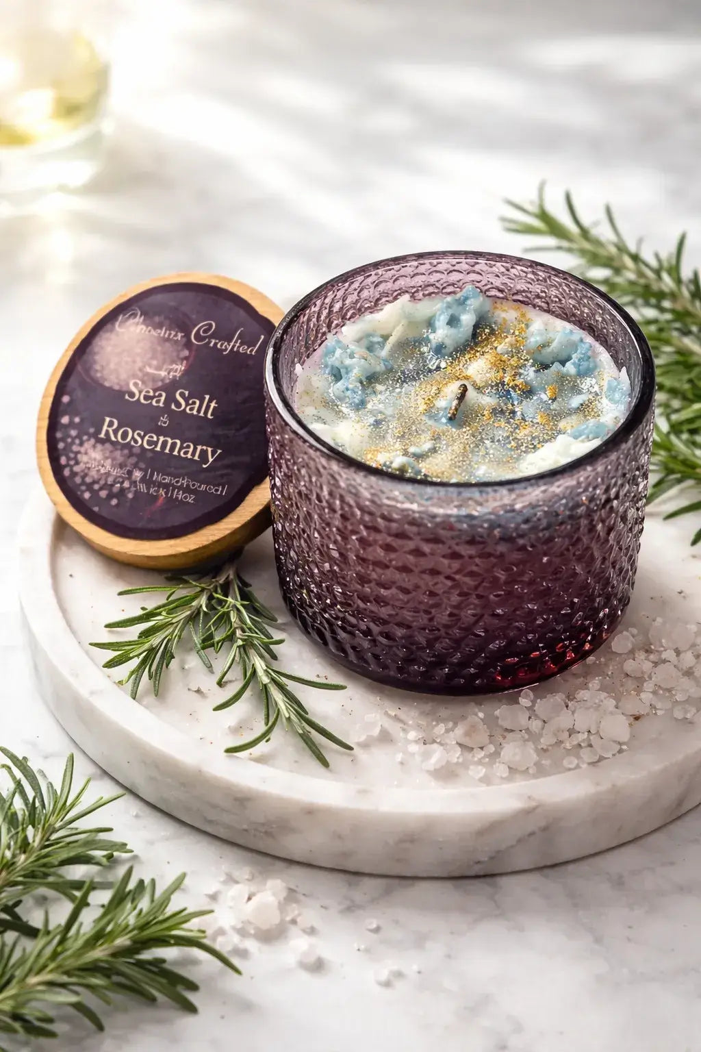 Sea Salt & Rosemary Candle in a textured glass holder on a marble surface, surrounded by fresh rosemary and sea salt.